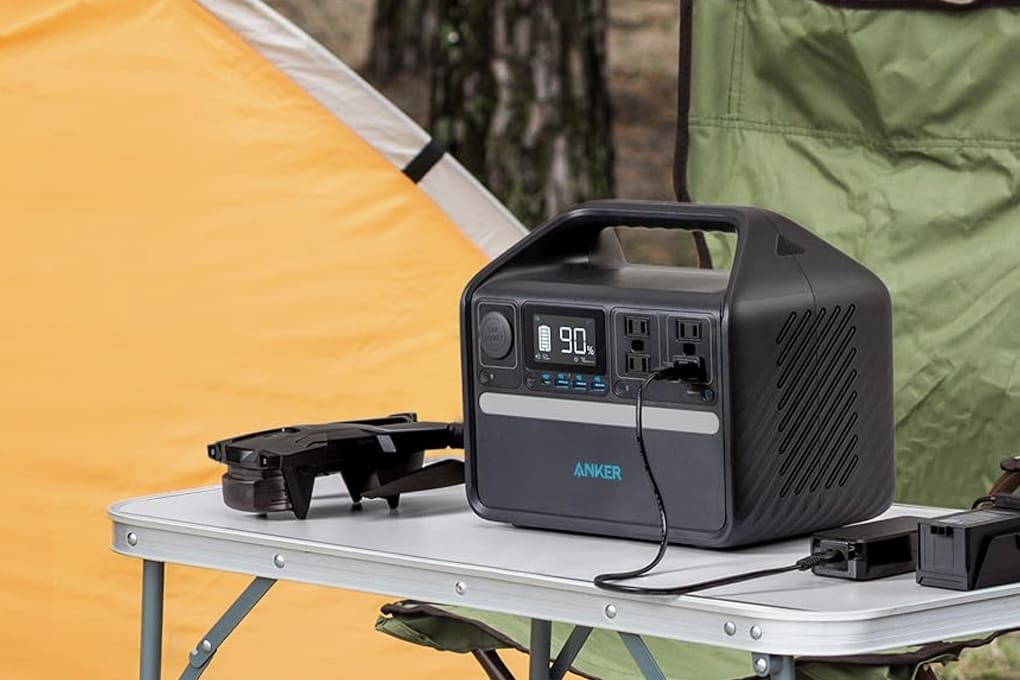 A Anker portable power station on a camping table beside an orange tent and green chair & the screen displays 90% charge