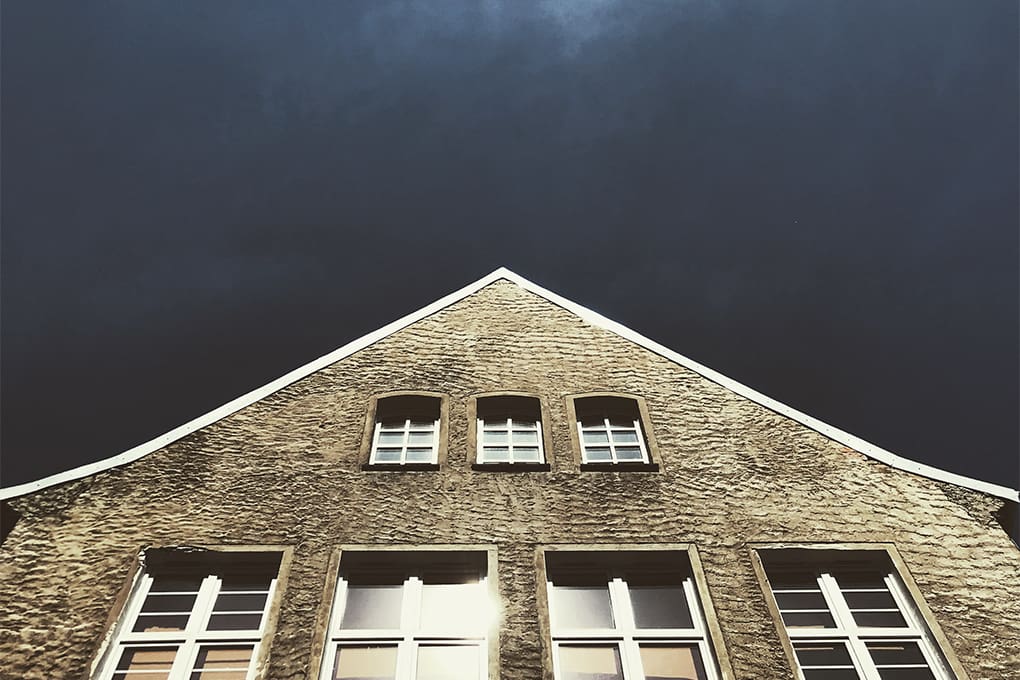 An upward view of a stone building with symmetrical windows against a dark sky, suggesting an impending hurricane storm