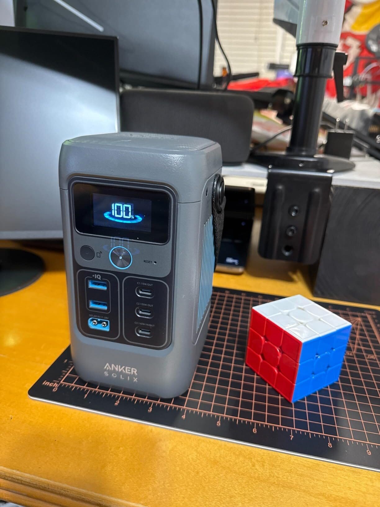 A Anker Solix C200 DC power station showing a 100% charge, sits on a desk with a Rubik's Cube next to it.